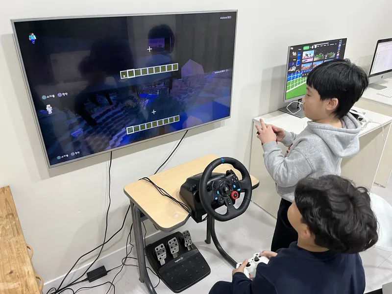 레이싱 휠과 게임 패드로 화면 속 게임을 함께 즐기는 아이들